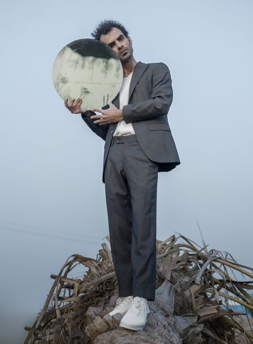 Free A man in a gray suit holding a round mirror outdoors. Low angle shot with a clear sky. Stock Photo