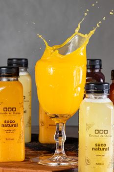 Dynamic splash of orange juice in a wineglass surrounded by natural juice bottles.