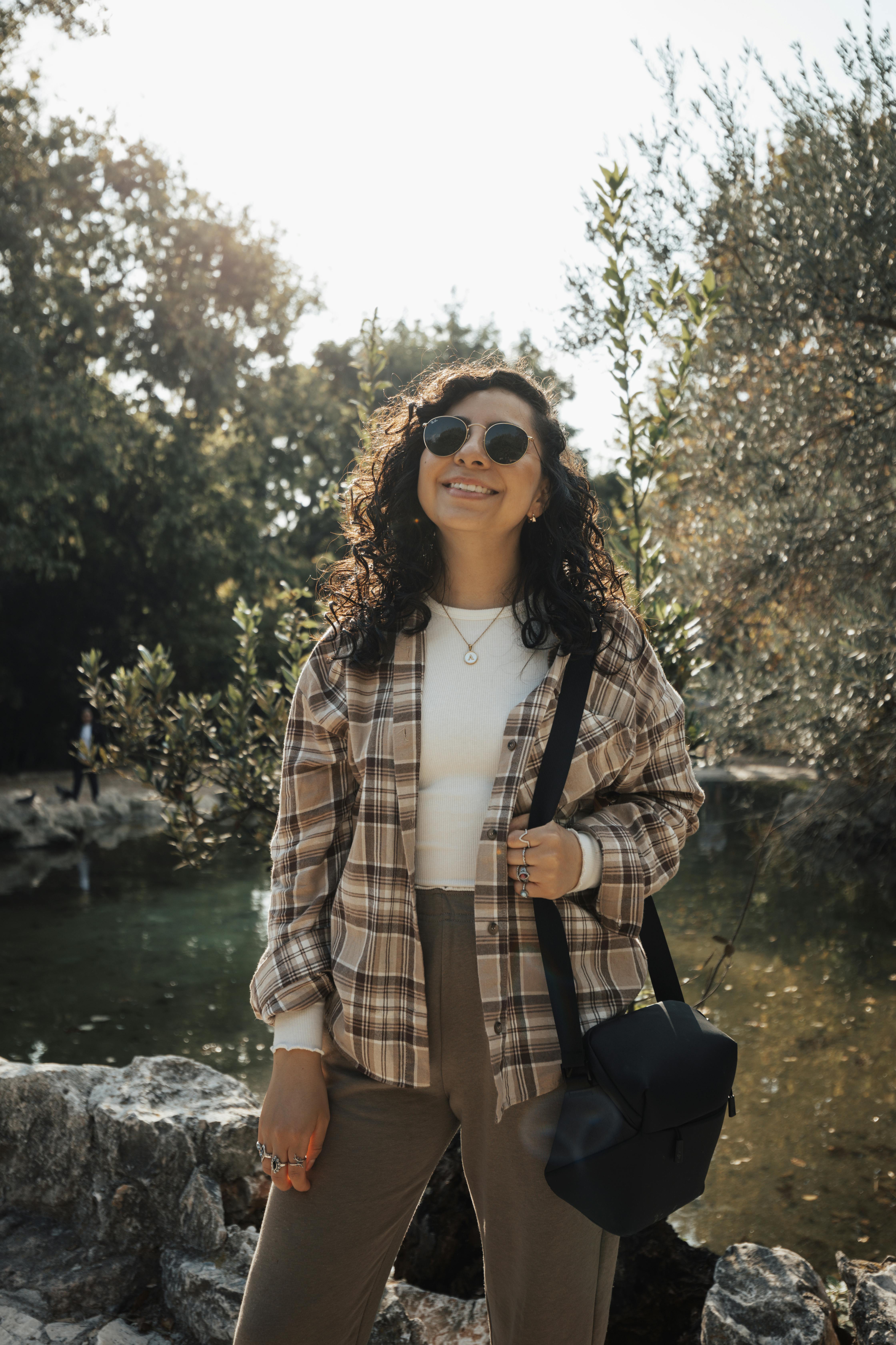 a woman in a plaid shirt and sunglasses standing by a river