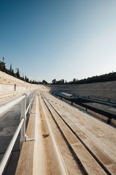 Sunlit view of the historic Panathenaic Stadium's empty bleachers with a clear blue sky backdrop.