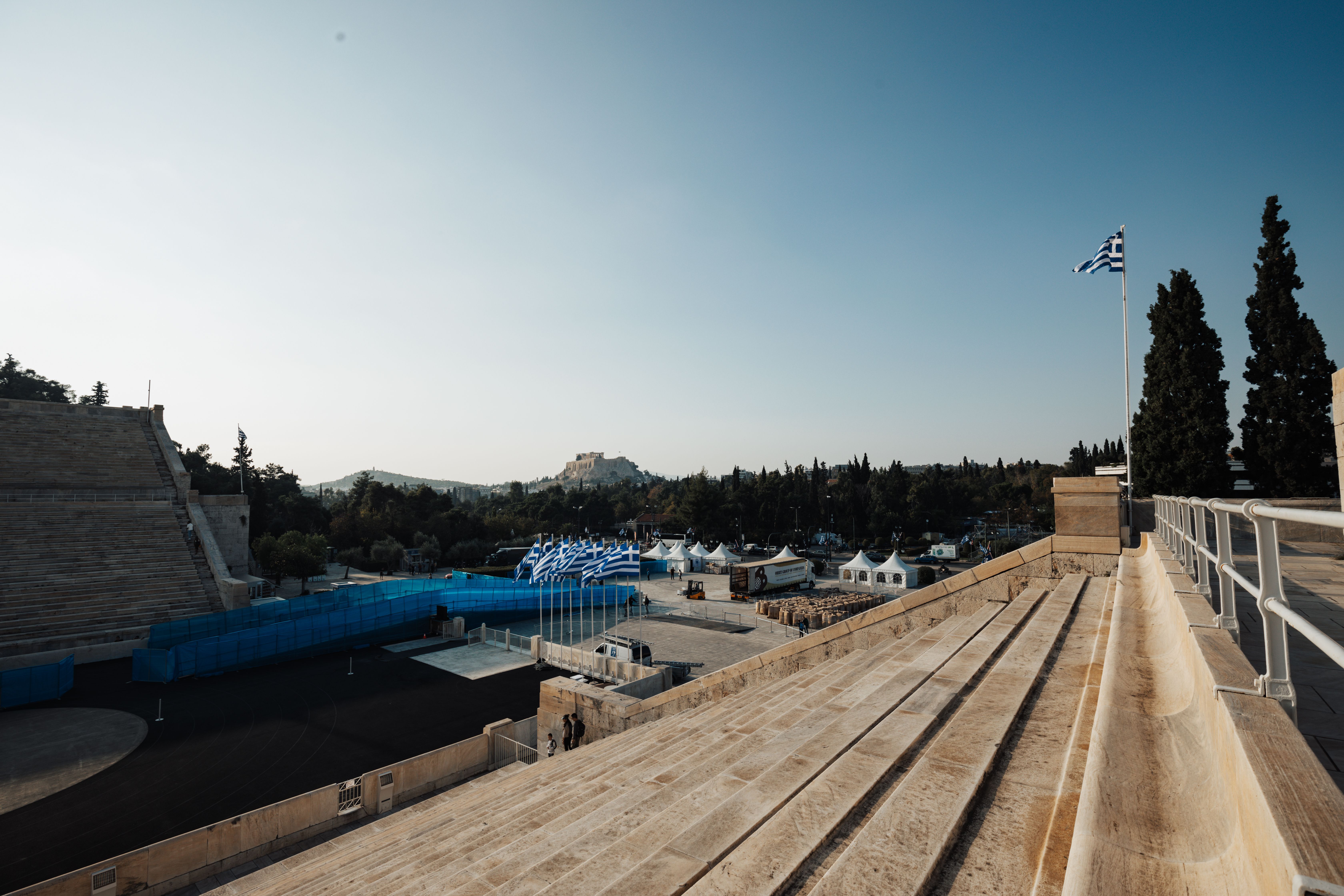 Panoramic image capturing the historic Panathenaic Stadium in Athens with the Greek flag and cityscape.