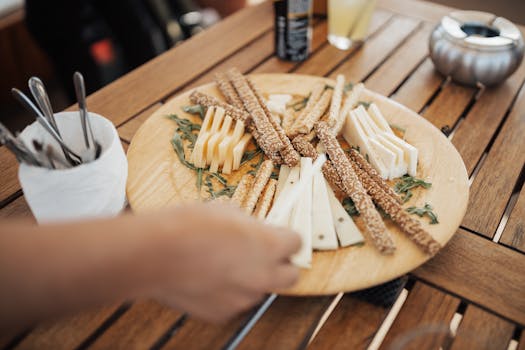 A wooden platter with assorted cheeses and sesame breadsticks on a wooden table.