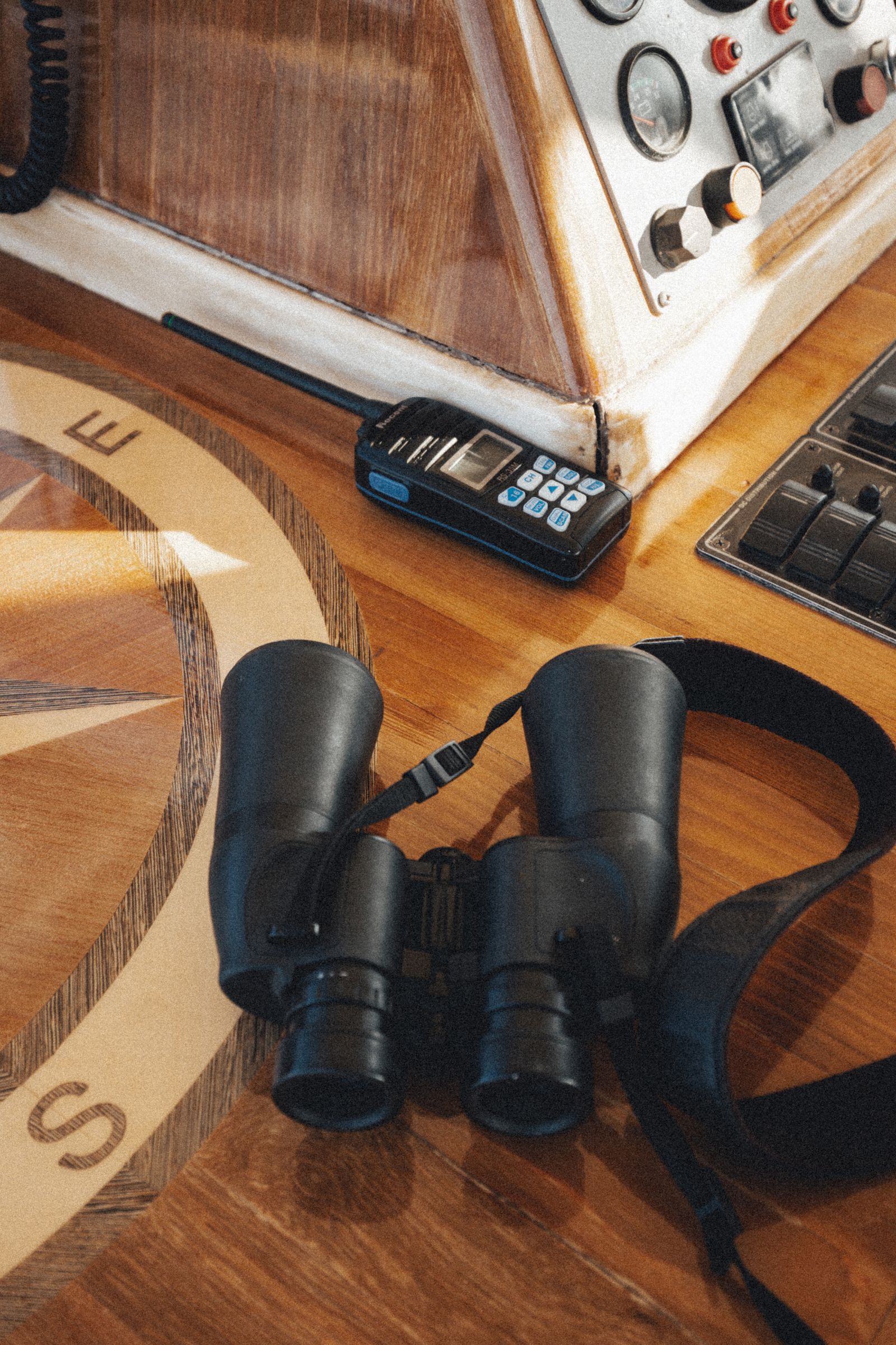 Nautical navigation tools including a compass and binoculars on a wooden table in a boat cockpit