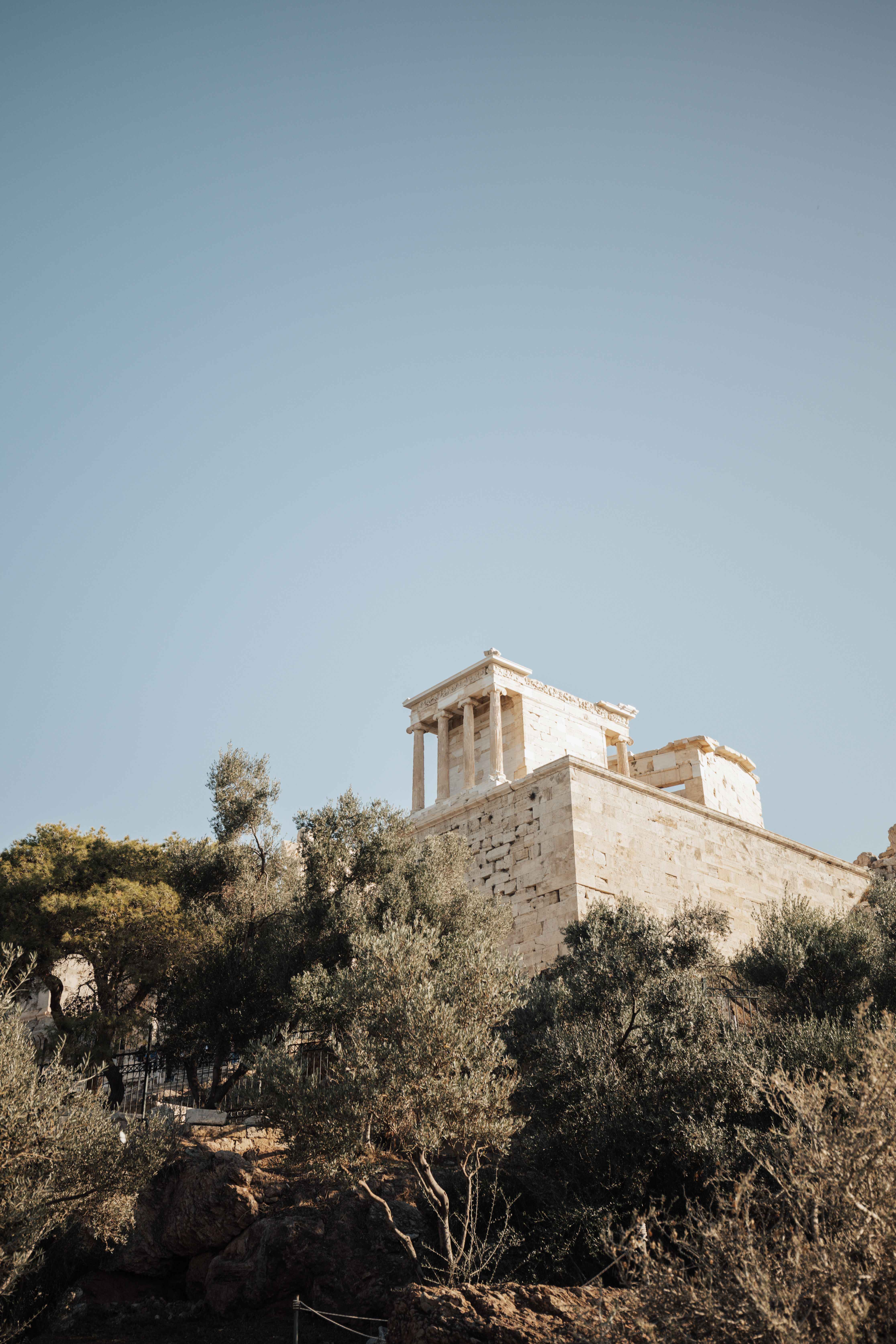 View of an ancient Greek temple surrounded by trees under a clear blue sky in Athens, Greece.