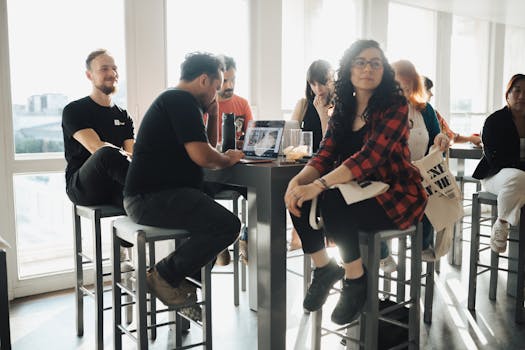 A group of adults gathered around a table with laptops in a modern office setting.