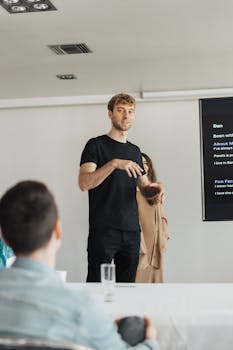 Young male professional giving a presentation to colleagues in a modern office setting.