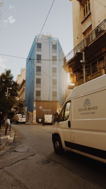 Urban street view featuring modern building facade with parked vans and pedestrians in warm lighting.