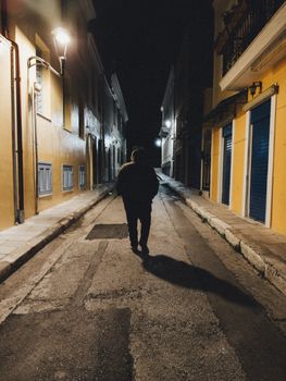 A person walks alone down a dimly lit urban alley at night.
