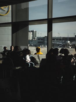Photo by Matheus Bertelli Silhouetted travelers in an airport terminal waiting area near large windows with outside tarmac view.