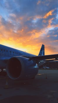 A commercial airplane parked on a tarmac with a stunning sunset backdrop in London.