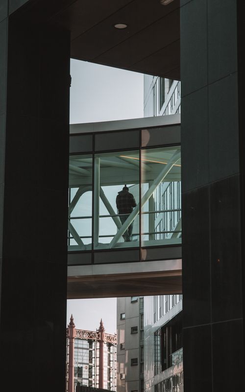 Free Silhouette of a person walking through a glass walkway amidst Dublin's modern architectural landscape. Stock Photo