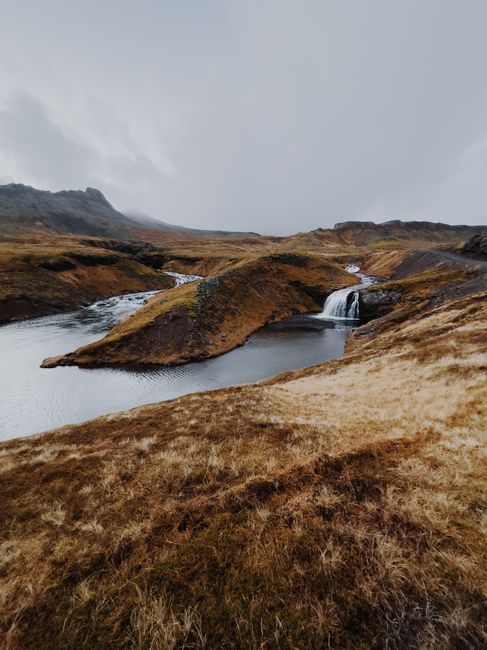 Breathtaking view of a tranquil waterfall with autumn foliage in Ólafsvík, Iceland.