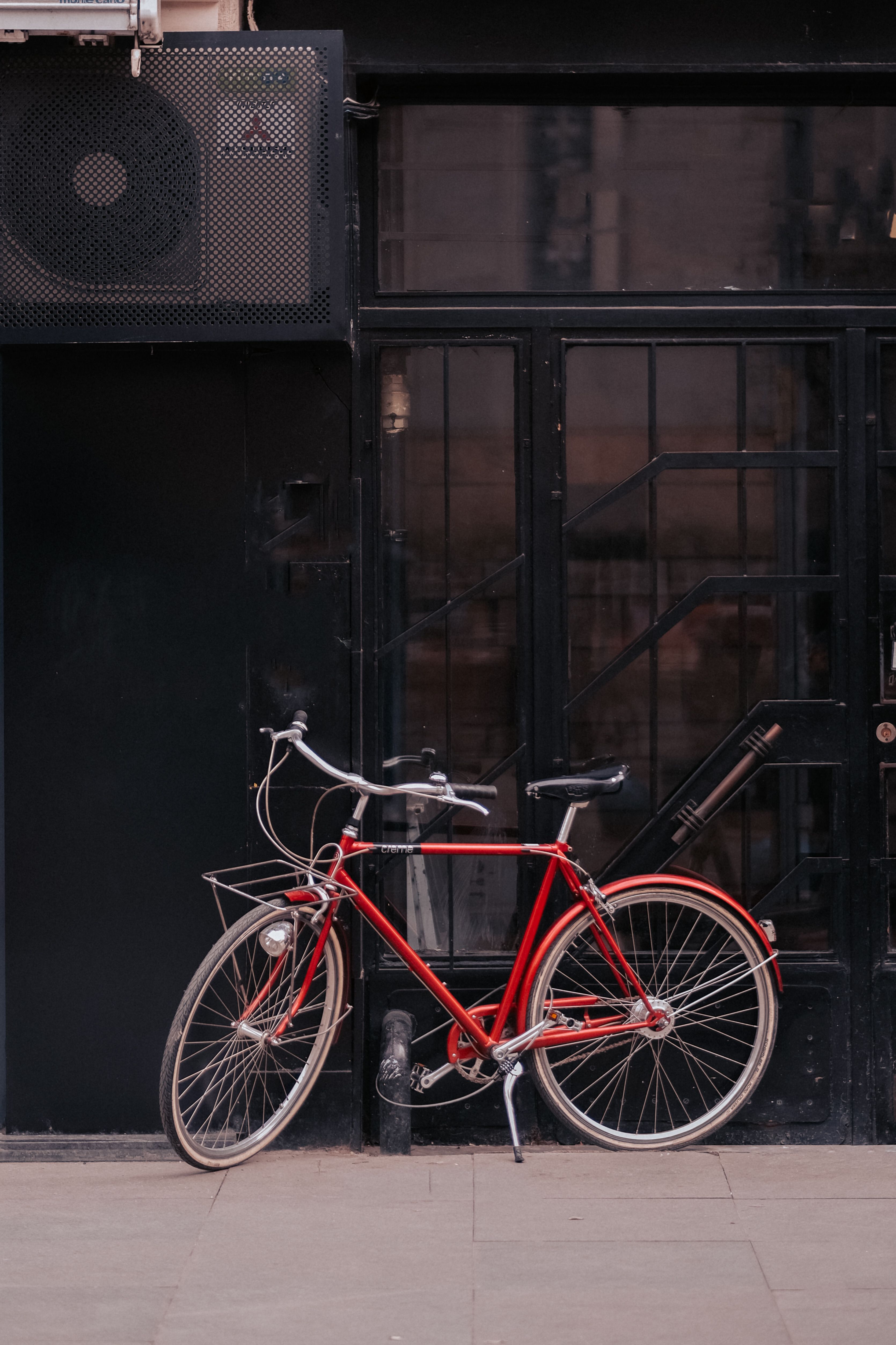 A vintage red bicycle rests against a black urban wall, contrasting with the city backdrop.