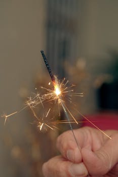 A hand holding a lit sparkler with bright sparks, symbolizing celebration.