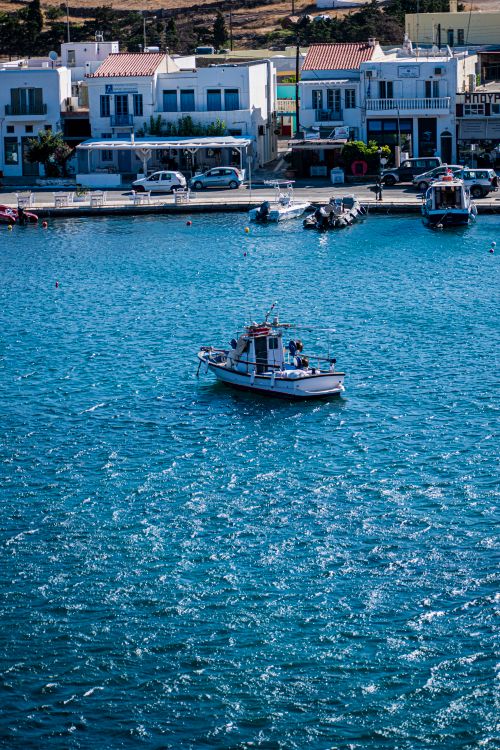 Free A small boat navigates a tranquil harbor, with scenic waterfront views. Ideal for travel and cityscape themes. Stock Photo