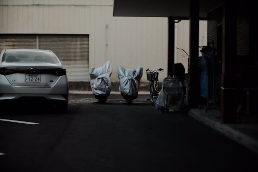 A dimly-lit urban parking lot featuring covered motorcycles and a parked car.