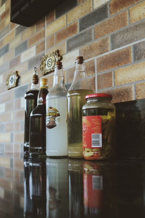 Free A rustic bar setup featuring vintage bottles and jars on a reflective counter against a brick wall. Stock Photo