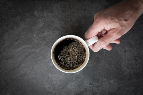 Free A hand grips a ceramic cup filled with black coffee on a gray surface. Stock Photo