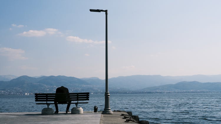 Back Of A Man Sitting On A Bench By A Streetlight On A Pier