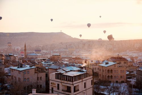 Free Scenic view of hot air balloons floating over Cappadocia at sunrise with snowy rooftops. Stock Photo