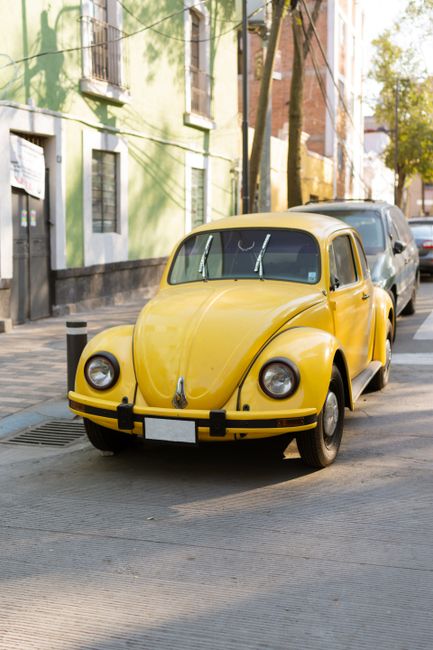 Classic Volkswagen Beetle in bright yellow, parked on a city street. Iconic vintage car in a vibrant urban setting.