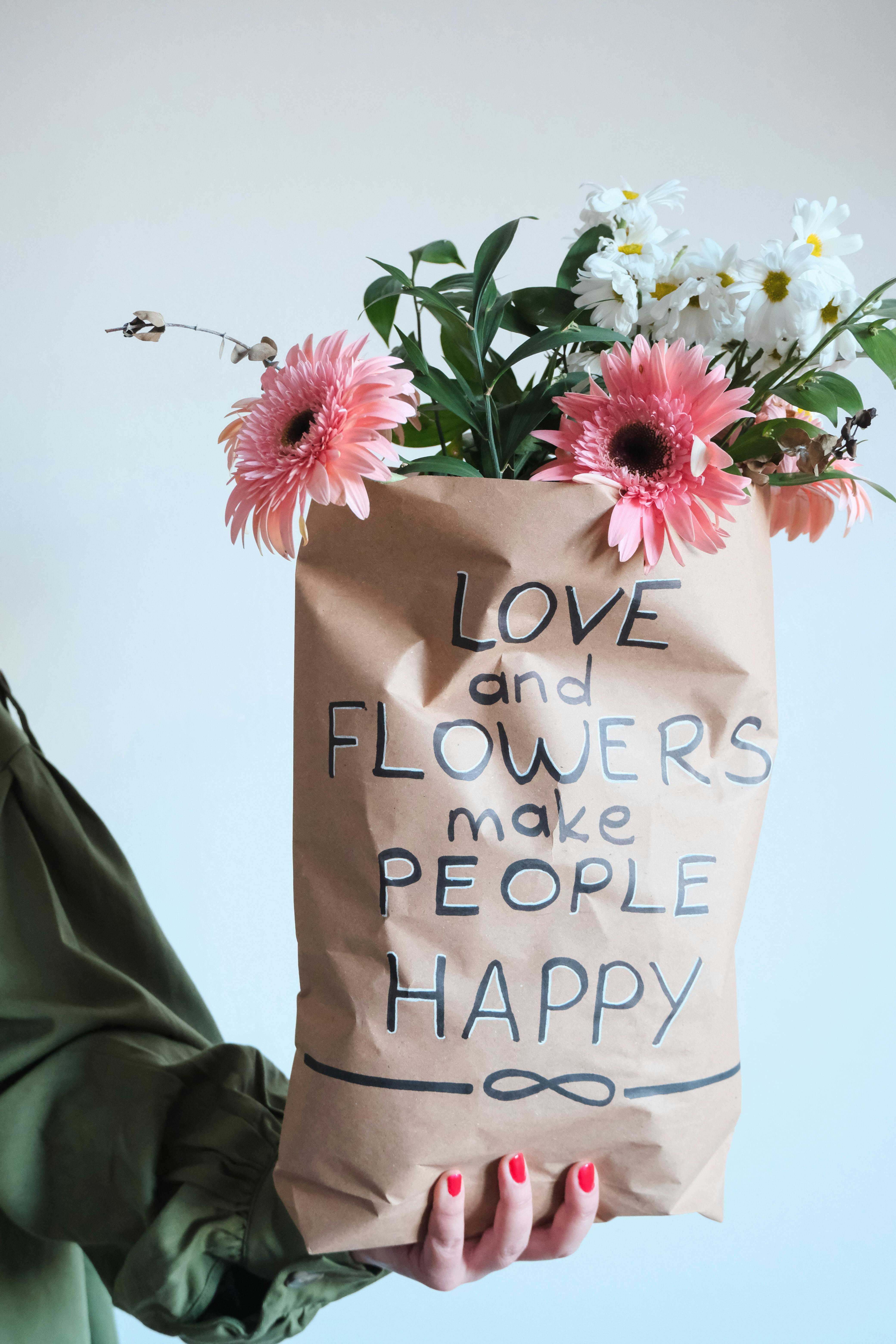 A hand holds a paper bag with flowers and inspiring text on a white background.