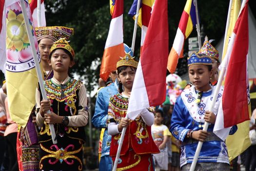 Children in colorful traditional clothing participate in a lively cultural parade, holding flags and celebrating their heritage.