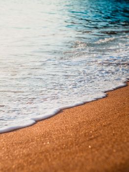 Sunlight glistens on a sandy beach with gentle waves, evoking a serene summer vibe.