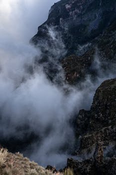 Dramatic view of a mountain range enveloped in dense fog and clouds.