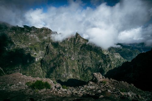 Free A breathtaking view of rugged mountains enveloped in clouds and lush greenery under a vibrant sky. Stock Photo