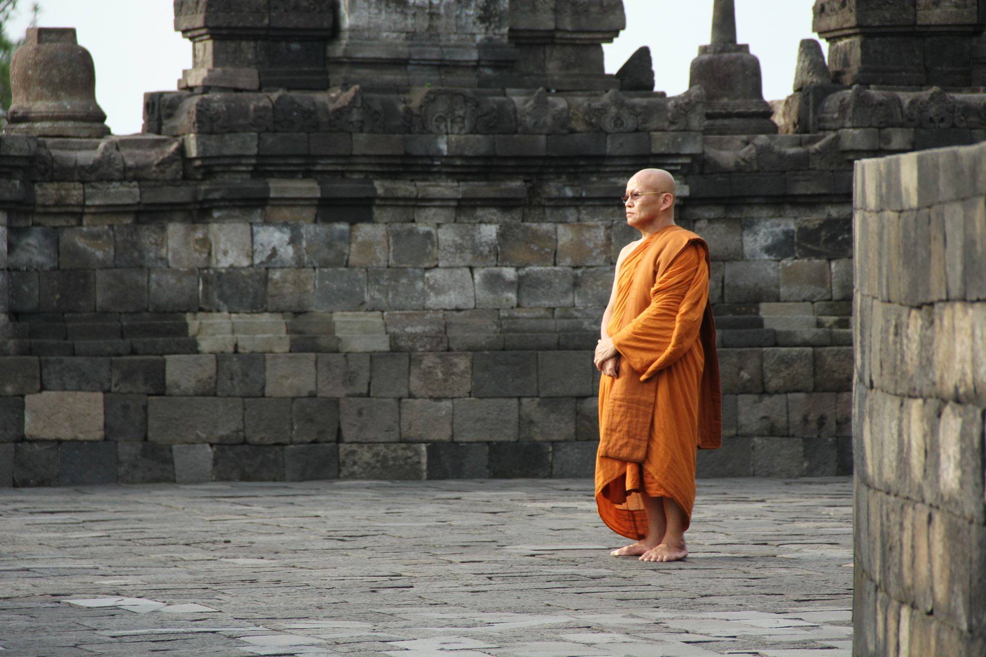 A Buddhist monk stands in orange robes at an ancient stone temple, depicting peace and spirituality.