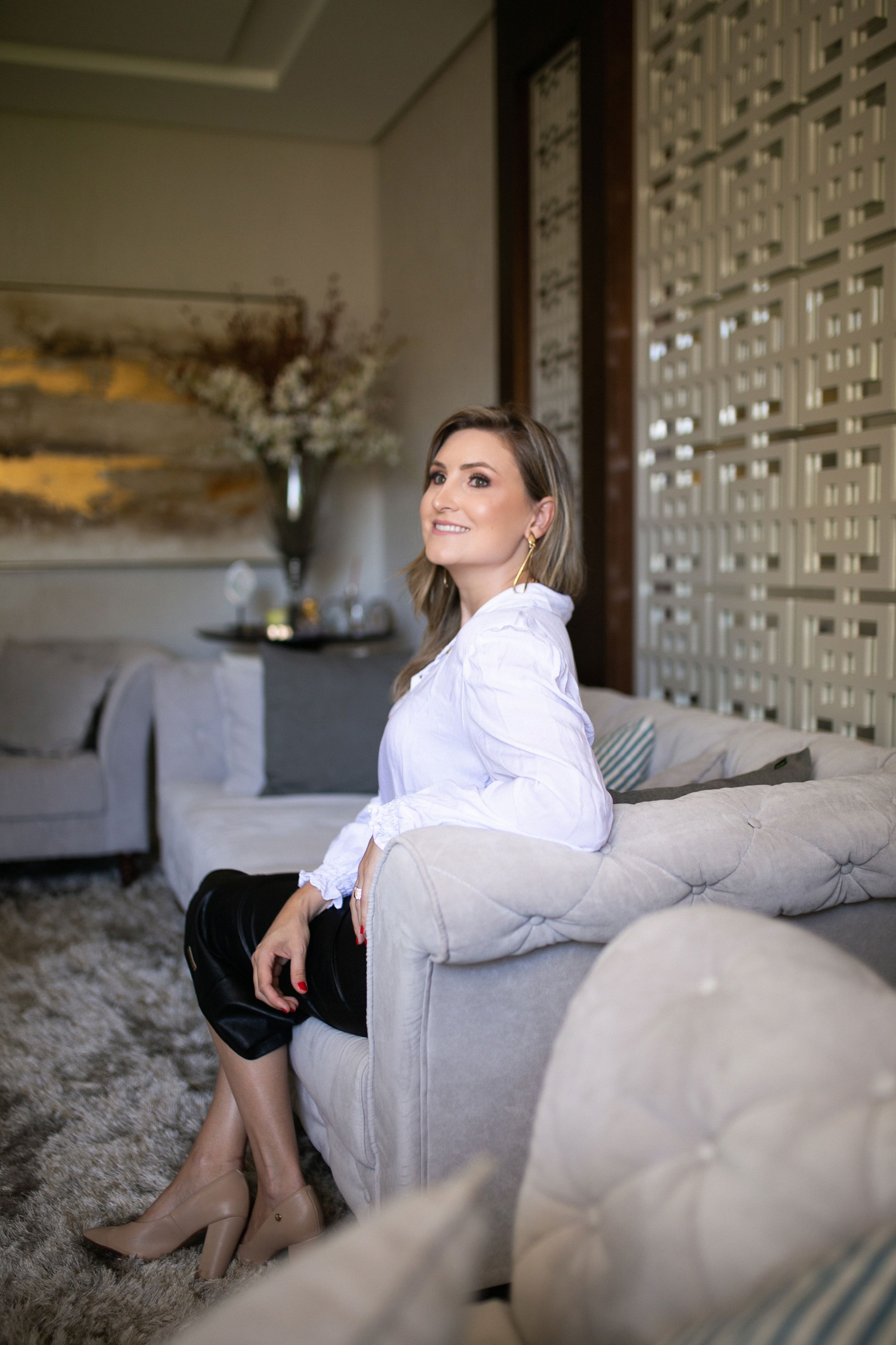 Stylish woman in a white blouse sitting on a couch in a modern living room.