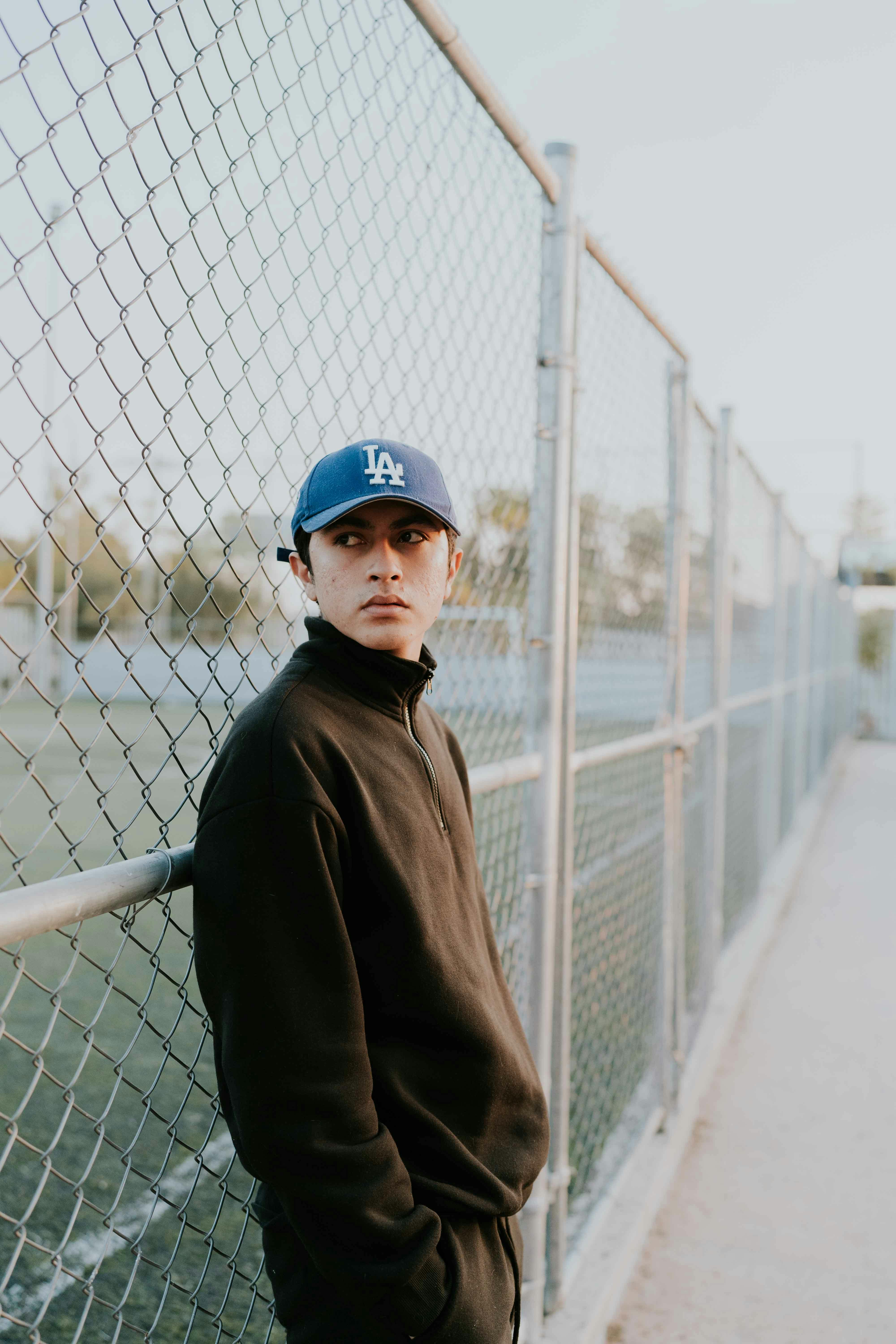 man in a sweatshirt and a cap by a chain link fence