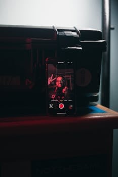 Close-up of a smartphone recording video, with a person displayed on the screen, in a dimly lit indoor setting.