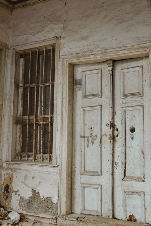 Free An abandoned old house with a weathered white wooden door and barred window. Stock Photo