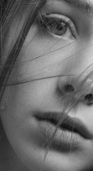 Artistic black and white close-up portrait of a woman's face, highlighting her eye and lips.