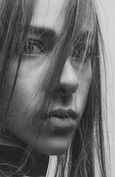 Close-up black and white portrait capturing the intense gaze of a woman with hair across her face.