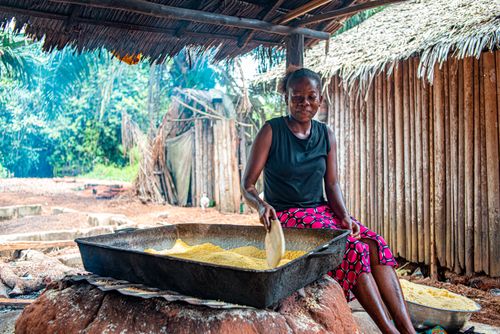 Free A woman smiles as she prepares cornmeal outdoors in a traditional village setting, capturing cultural authenticity. Stock Photo