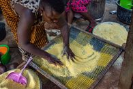 A woman works with a sieve to prepare traditional African maize meal outdoors.