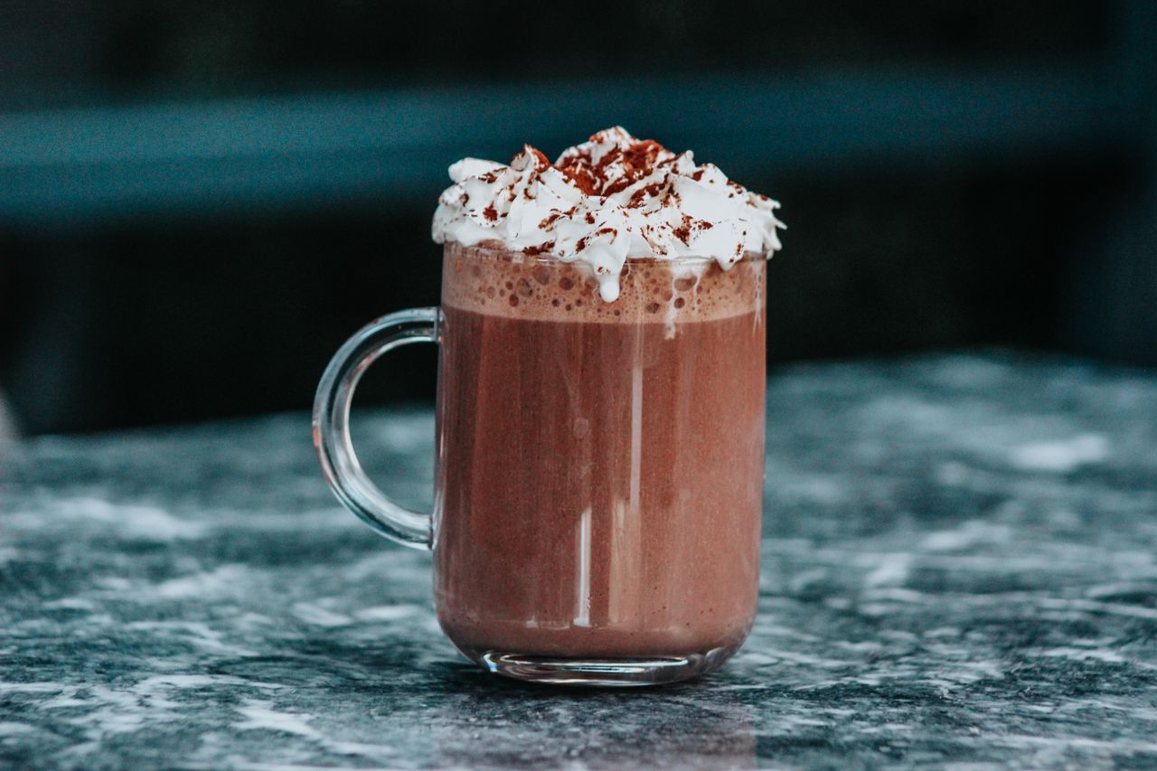 Hot chocolate with whipped cream in a clear glass mug on marble