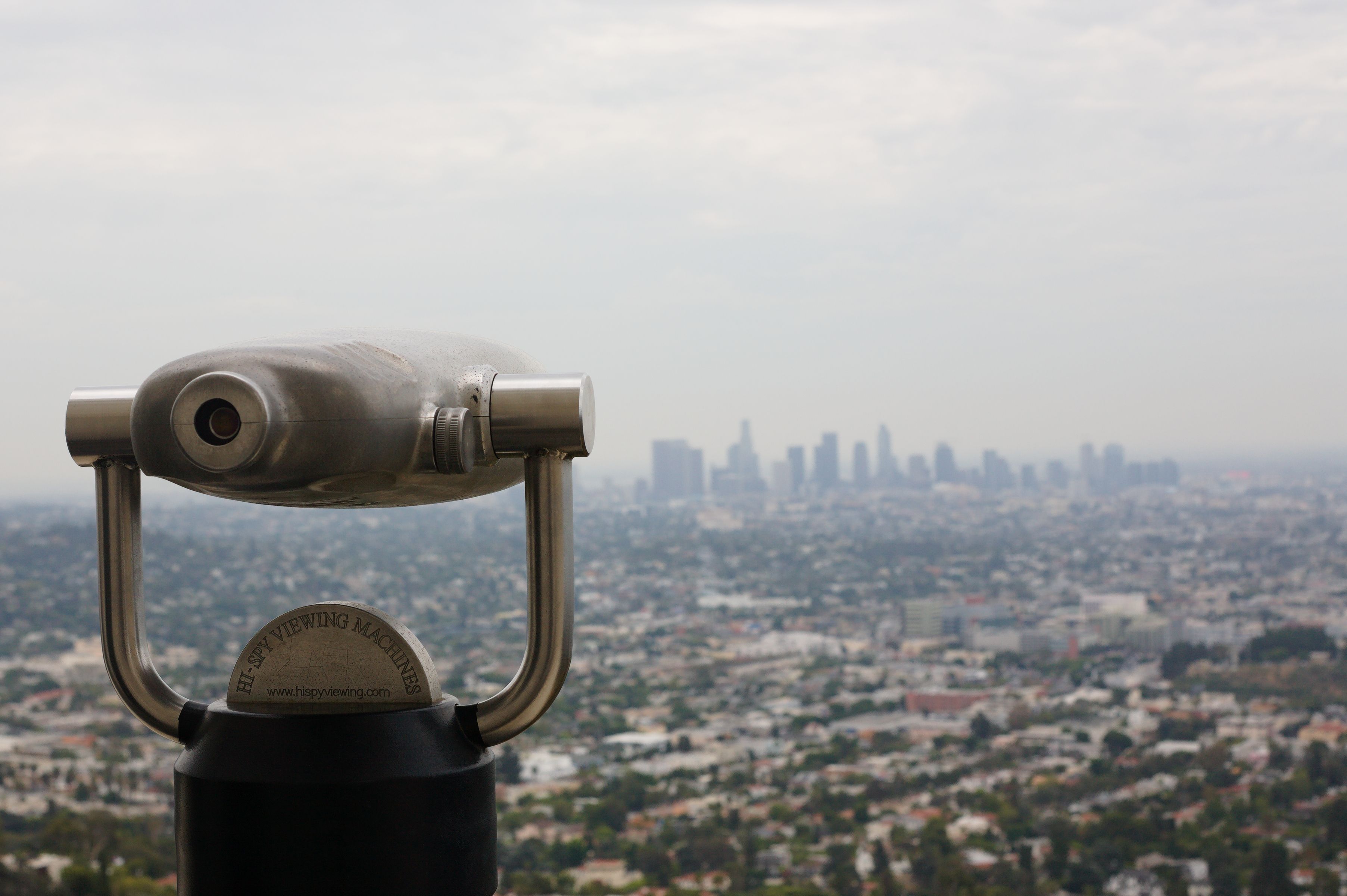 Cityscape featuring a telescope overlooking a sprawling urban skyline under a cloudy sky.