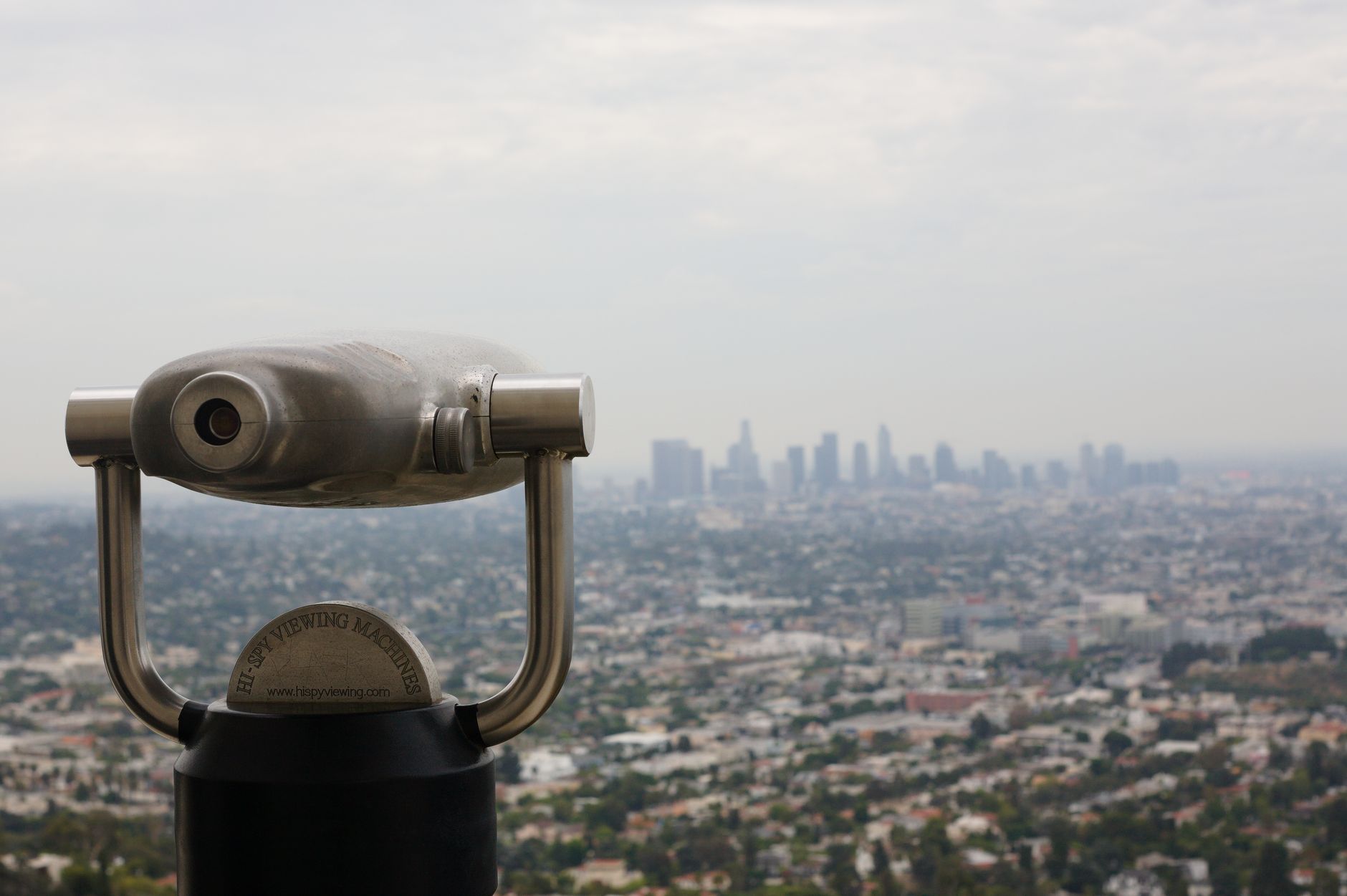 Cityscape featuring a telescope overlooking a sprawling urban skyline under a cloudy sky.