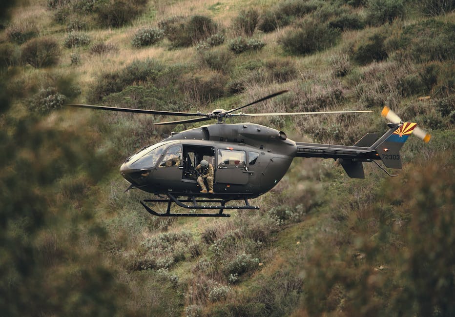 A military helicopter transports soldiers over a rugged, grassy landscape on an operation.