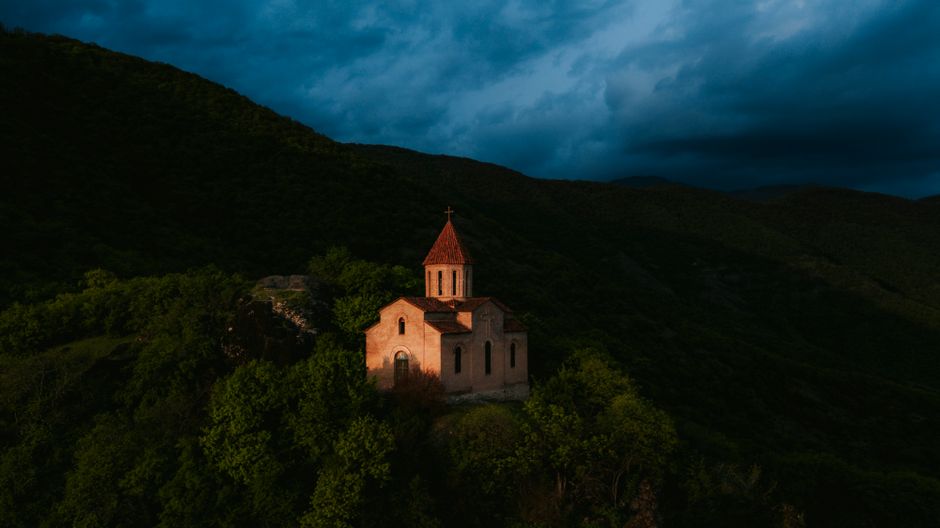 Aerial view of a solitary church on a mountain against a dramatic evening sky.