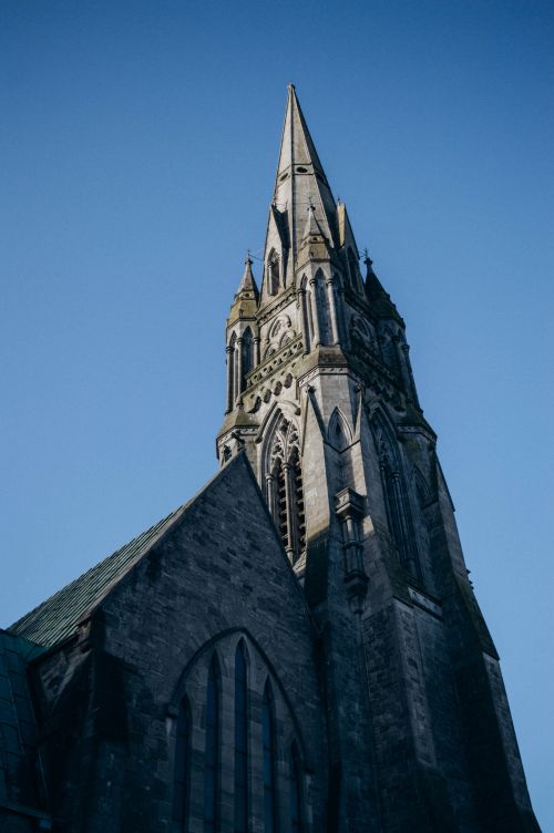 Free A stunning low angle view of a gothic cathedral tower set against a clear blue sky, highlighting intricate architecture. Stock Photo