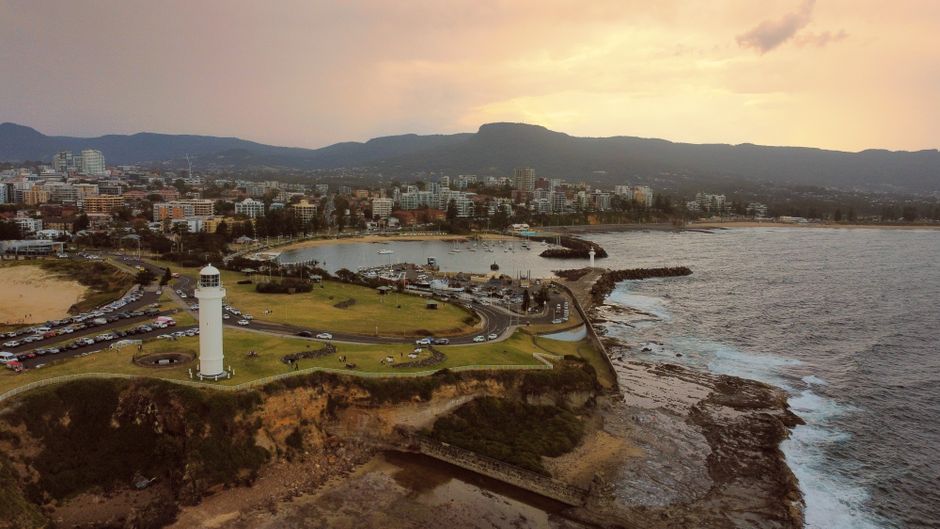 30-Minute Sydney Harbour and Olympic Park Helicopter Tour - Aerial view of Wollongong cityscape with a prominent lighthouse and coastline at sunset.