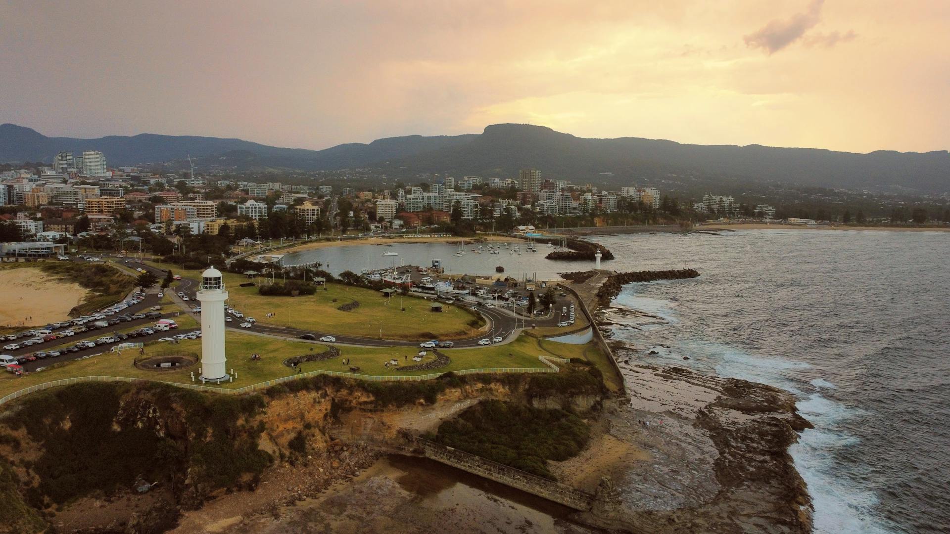 Aerial view of Wollongong cityscape with a prominent lighthouse and coastline at sunset.
