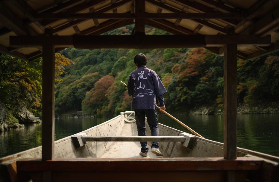 A lone man stands on a boat in a serene river surrounded by lush trees in Katsuura, Japan.