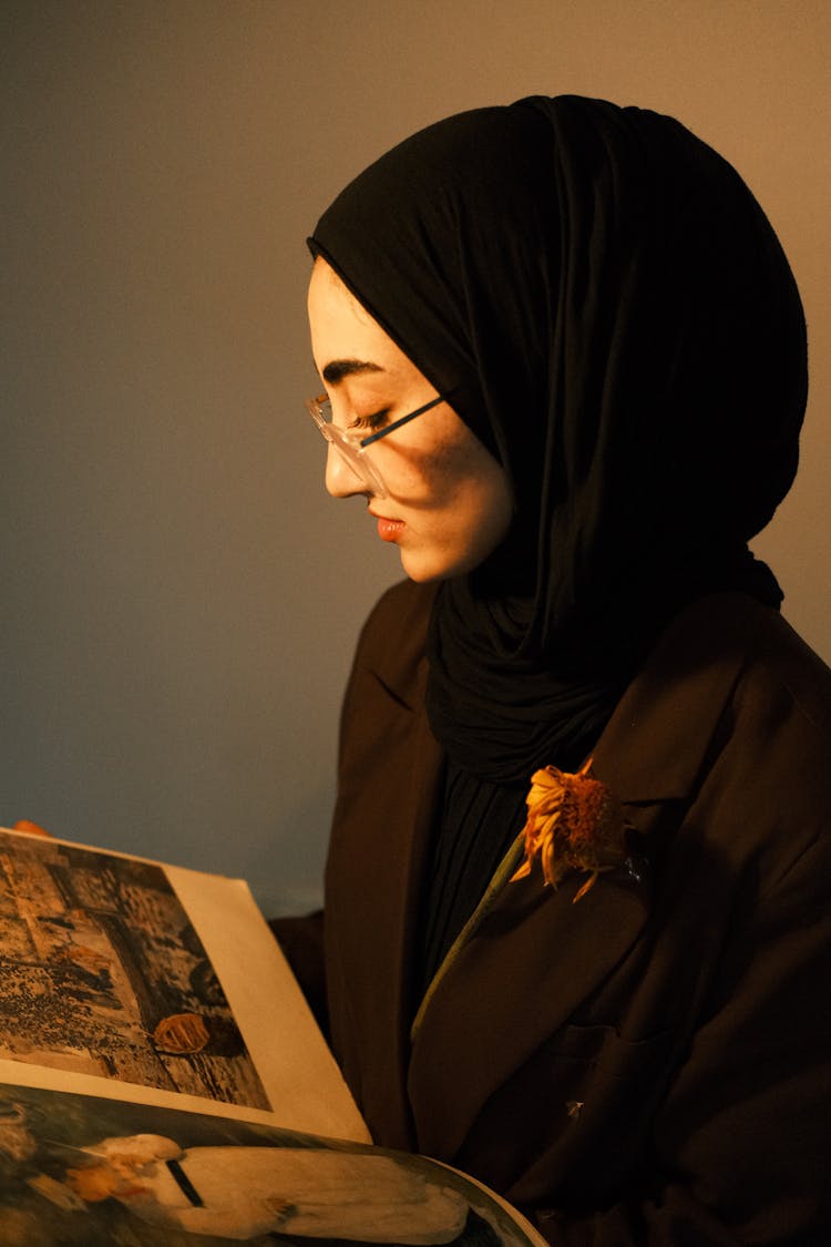 A Woman In Black Hijab Looking At The Magazine She Is Holding