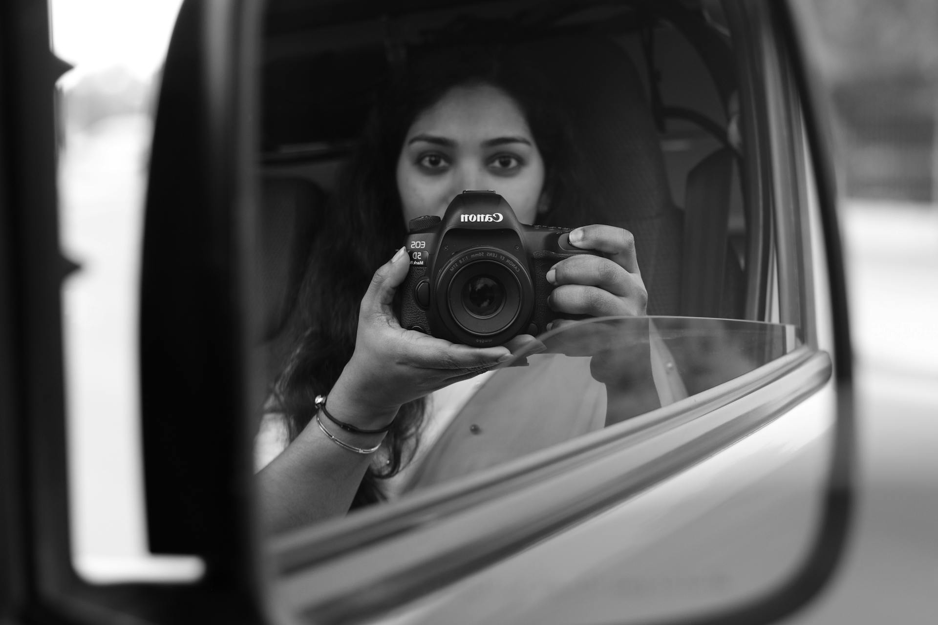 Artistic black and white reflection photo of a woman with a camera in a car side mirror, captured in Manama, Bahrain.